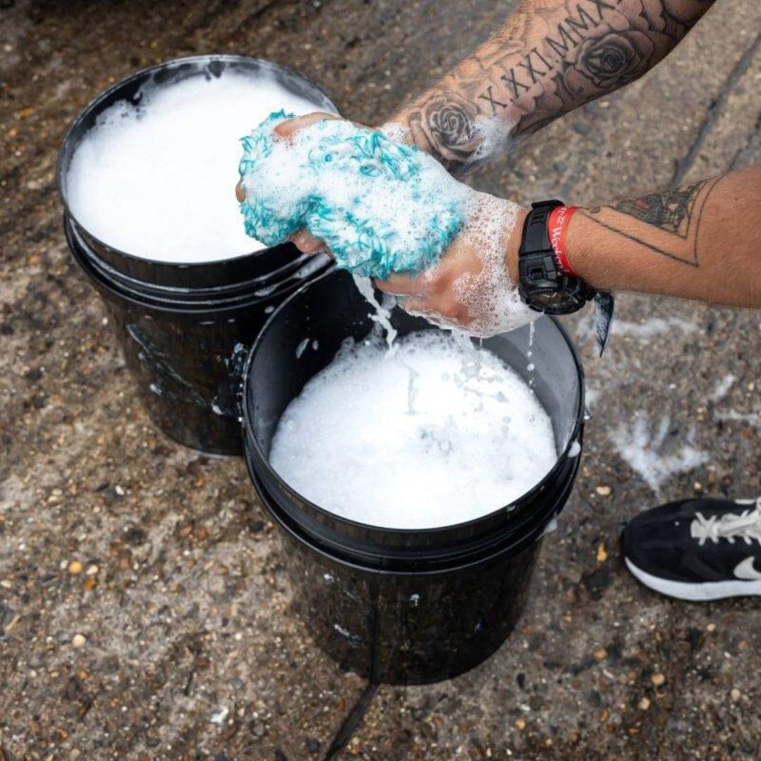 Pessoa utilizando dois baldes com grelha para lavagem de carros, destacando o uso eficiente de água e produtos de limpeza para um acabamento perfeito.